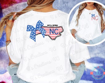 May include: White t-shirt featuring a red, white and blue bow and an outline of North Carolina with the letters "NC" in blue. The text "North Carolina" is written above the state outline.