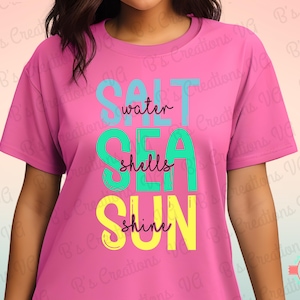 May include: A pink t-shirt with the words "SALT SEA SUN" in turquoise, green, and yellow. The words "water", "shells", and "shine" are written in a script font. The shirt is a crew neck and short-sleeved.