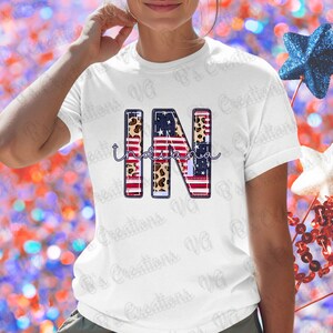 May include: White t-shirt with the letters "IN" in an American flag and leopard print design, with "Indiana" written below. The design is a patriotic theme. The shirt is a casual wear item.