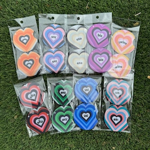 May include: Twelve sets of colorful heart-shaped car coasters with different band names printed on them. The coasters are packaged in clear plastic bags.