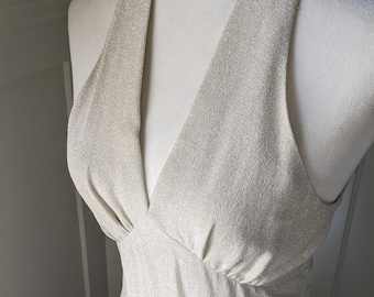May include: A sleeveless, sparkly, silver dress with a deep V-neckline. The dress has a fitted bodice and a flowing skirt.