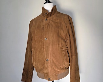 May include: A brown suede jacket with a high collar and button closure. The jacket has a ribbed hem and cuffs. The jacket is displayed on a mannequin. The jacket is a medium brown color.