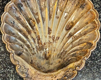 Könnte beinhalten: Eine silberne Muschelformschale mit einem verzierten Design am Rand. Die Schale ist leicht angelaufen und hat einen Vintage-Look.