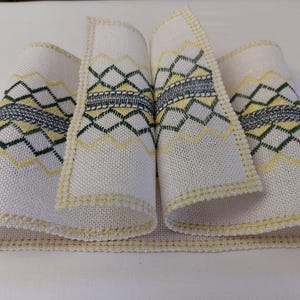 May include: A white fabric ribbon with a yellow, green, and gray geometric pattern. The ribbon has a scalloped edge.