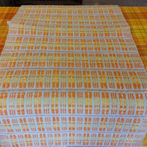 May include: A woven table runner with a geometric pattern in shades of orange and beige.