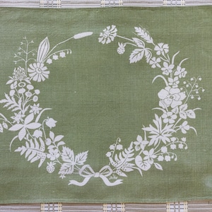 Peut inclure: Set de table en lin vert avec un motif de couronne de fleurs blanches. La couronne est composée de différentes fleurs, feuilles et baies.