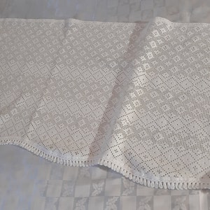 May include: White crocheted lace tablecloth with a diamond pattern and fringe trim.
