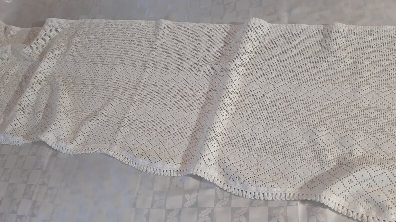 May include: White crocheted lace tablecloth with a diamond pattern and fringe trim.