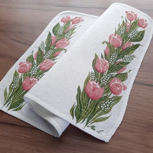 May include: Two white linen tea towels with a pink and green floral design. The towels feature a repeating pattern of tulips and leaves.