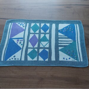 Puede incluir: Un camino de mesa azul y blanco con estampado geométrico y borde azul claro. El patrón presenta triángulos, cuadrados y rombos.