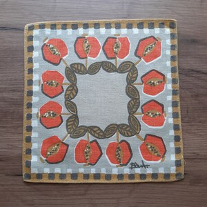 May include: A square, gray linen napkin with a black and white checkered border. The napkin features a repeating pattern of stylized red fruit with black seeds and brown leaves.