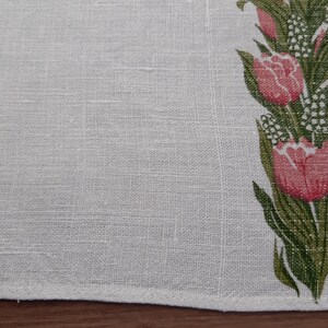 May include: White linen tea towel with a green and pink floral design. The design features tulips and small white flowers. The towel is signed "Mia L."