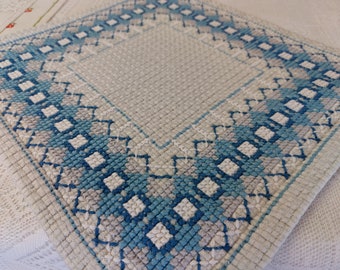 May include: A white crocheted placemat with a blue and gray geometric border.