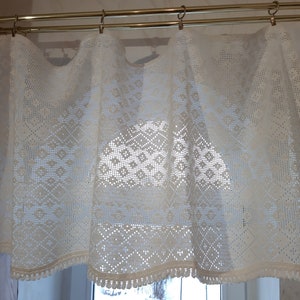May include: White crocheted valance with a diamond pattern and a fringe trim. The valance is hung on a double rod.