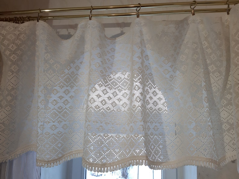 May include: White crocheted valance with a diamond pattern and a fringe trim. The valance is hung on a double rod.