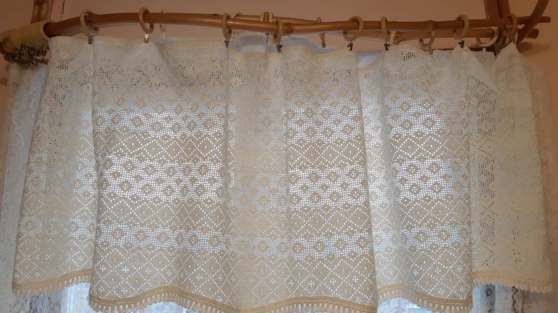 May include: White crocheted valance with a diamond pattern, hanging on a wooden rod.