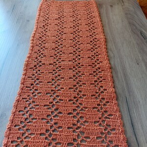 May include: A crocheted table runner in a burnt orange color with a diamond pattern.