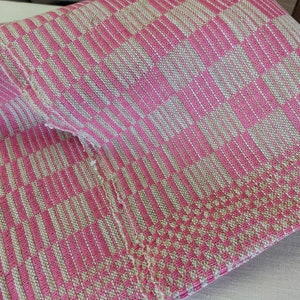 Peut inclure: Tissu tissé rose et beige à motif à carreaux. Le tissu est plié en deux et les bords sont effilochés.