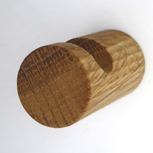 May include: A wooden phone stand, crafted from a light brown, cylindrical piece of wood. It features a curved groove at the top for holding a phone. The visible wood grain enhances the natural appearance of the stand.
