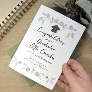 May include: A graduation card with floral detailing and the text "Congratulations on your Graduation Ellie Coombes." The card includes the University of Nottingham and the year 2026. The card is held in a hand.