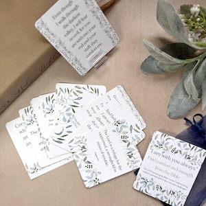 May include: A collection of Bible verse cards with floral borders. The cards display inspirational quotes and text. A pen and decorative greenery are also visible in the image.