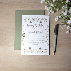 May include: A birthday card with the message "Happy Birthday to a special friend" in elegant script, surrounded by floral illustrations. A matching green envelope and a pen are next to the card. White flowers are in the background.