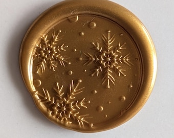 May include: A gold wax seal with a snowflake design. The seal is round and has a raised edge.