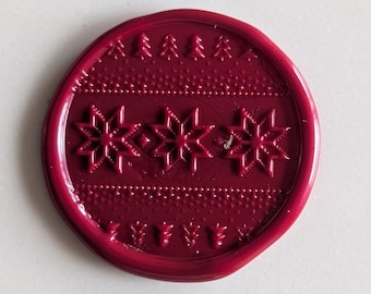 May include: A red wax seal with a snowflake pattern. The seal has a raised design of three snowflakes and a border of small pine trees.