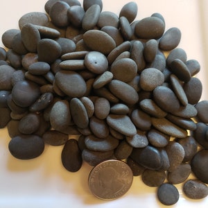 May include: A pile of smooth, dark gray river rocks, some oval-shaped, some round, with a US quarter for scale.