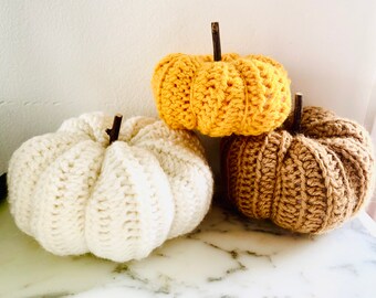May include: Three crocheted pumpkins in white, yellow, and brown. The pumpkins are made with a textured stitch and have a rustic, handmade look.