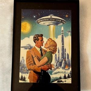 May include: Framed retro art print depicting a couple embracing under a starry sky with a UFO hovering above. The artwork features a futuristic city, a full moon, and a vintage aesthetic, all within a black frame.