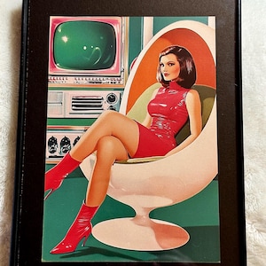 May include: Framed retro art print featuring a woman in a red dress and boots, seated in a white egg chair. The background includes a vintage green television and a mid-century modern design.