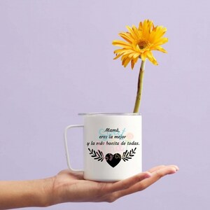 May include: White ceramic mug with a black handle and a floral design. The mug has the text "Mam&aacute;, eres la mejor y la m&aacute;s bonita de todas." with a heart in the center.