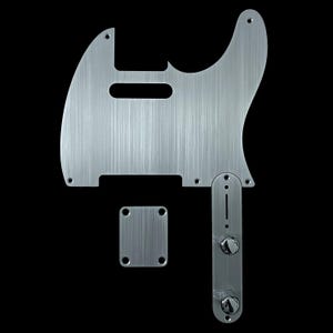 May include: Silver-colored guitar parts set against a black background. The set includes a pickguard, control plate, and neck plate. The pickguard has a rectangular cutout and several screw holes. The control plate features two knobs. The parts have a brushed metal finish.