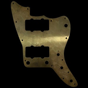 Op de afbeelding: Een gouden metalen gitaar pickguard met twee pick-up uitsparingen en meerdere schroefgaten.