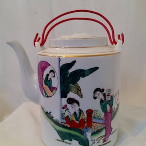 May include: White porcelain teapot with a red handle and a painted design of three women in a garden setting. The teapot has a gold trim around the lid and base.