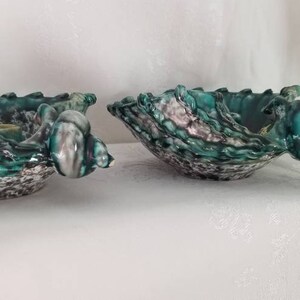 May include: Two green and white ceramic bowls with a textured, shell-like design. The bowls are shaped like seashells and have a glossy finish.