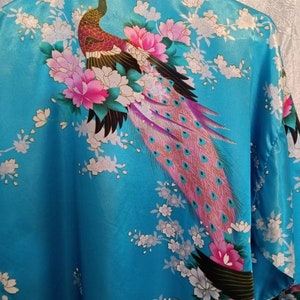 May include: A blue satin robe with a peacock and floral print. The peacock has a pink, purple, and green tail. The flowers are pink and white.