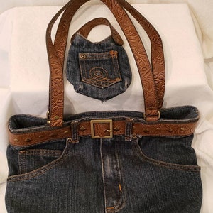 May include: A denim tote bag with brown leather straps and a matching belt. The bag has a small denim pouch attached to the front.