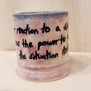 May include: A white ceramic mug with a blue and pink watercolor design. The mug has a quote written on it: "Your reaction to a situation has the power to change the situation itself."