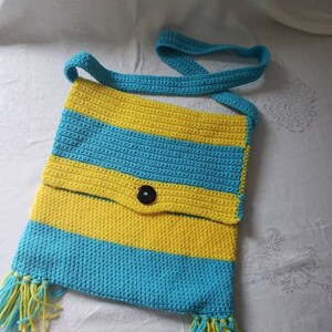 May include: A crocheted striped shoulder bag with yellow and blue stripes and a brown button. The bag has tassels on the bottom.