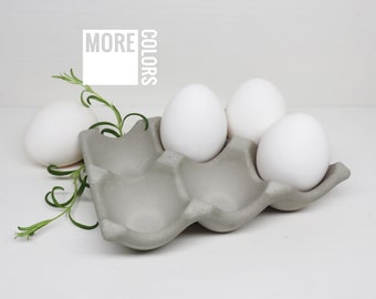 May include: A gray concrete egg carton with the words "More Colors" printed on it. Three white eggs are in the carton.