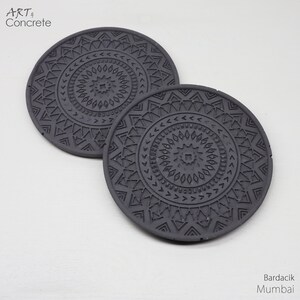 Puede incluir: Dos posavasos de hormig&oacute;n gris con un patr&oacute;n geom&eacute;trico. Los posavasos tienen un dise&ntilde;o de mandala con un cuadrado central y c&iacute;rculos conc&eacute;ntricos de tri&aacute;ngulos y puntos.