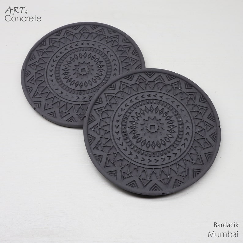 Puede incluir: Dos posavasos de hormig&oacute;n gris con un patr&oacute;n geom&eacute;trico. Los posavasos tienen un dise&ntilde;o de mandala con un cuadrado central y c&iacute;rculos conc&eacute;ntricos de tri&aacute;ngulos y puntos.