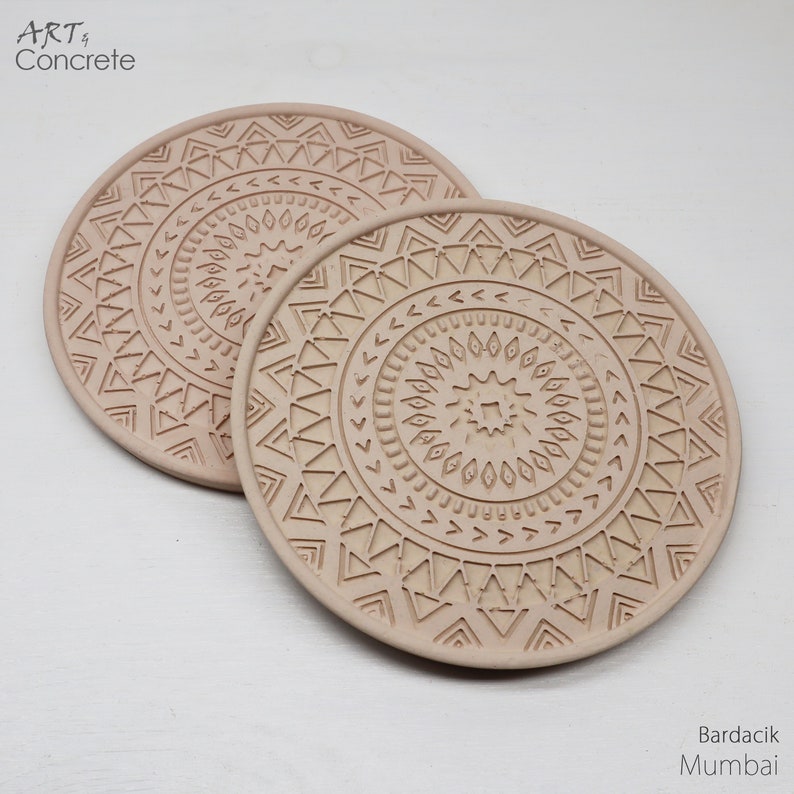 Puede incluir: Dos posavasos de hormig&oacute;n beige con un patr&oacute;n geom&eacute;trico. Los posavasos presentan un dise&ntilde;o circular con c&iacute;rculos conc&eacute;ntricos y tri&aacute;ngulos.