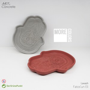 May include: Two concrete hand-shaped trays with an intricate design. One tray is gray and the other is red. The trays are both decorated with a paisley pattern and an eye in the center. The text "MORE COLORS" is visible in the background.