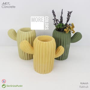 Può includere: Tre vasi a forma di cactus nei toni del giallo e del verde. I vasi hanno una consistenza a coste e sono riempiti di fiori secchi. Il testo "MORE COLORS" è visibile sull'immagine.