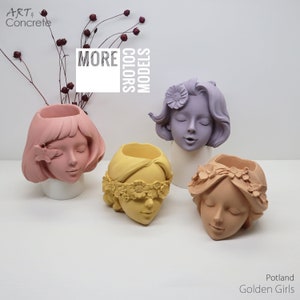 Op de afbeelding: Vier betonnen plantenbakken in de vorm van vrouwelijke gezichten. De potten zijn in verschillende kleuren geverfd: roze, geel, paars en oranje. De potten zijn op een wit oppervlak gerangschikt. De tekst "More Colors Models" is zichtbaar op de achtergrond.