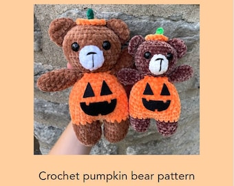 May include: Two crocheted brown teddy bears dressed as pumpkins. The larger bear is holding a smaller bear in its arms. Both bears have black eyes and a black stitched smile. The bears are wearing orange pumpkin costumes with green stems and black jack-o-lantern faces.
