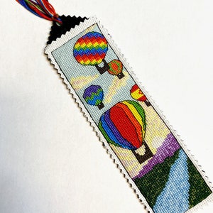 May include: A colourful bookmark with a stitched design of hot air balloons in a sky with clouds. The bookmark has a black tassel with multi-coloured threads.
